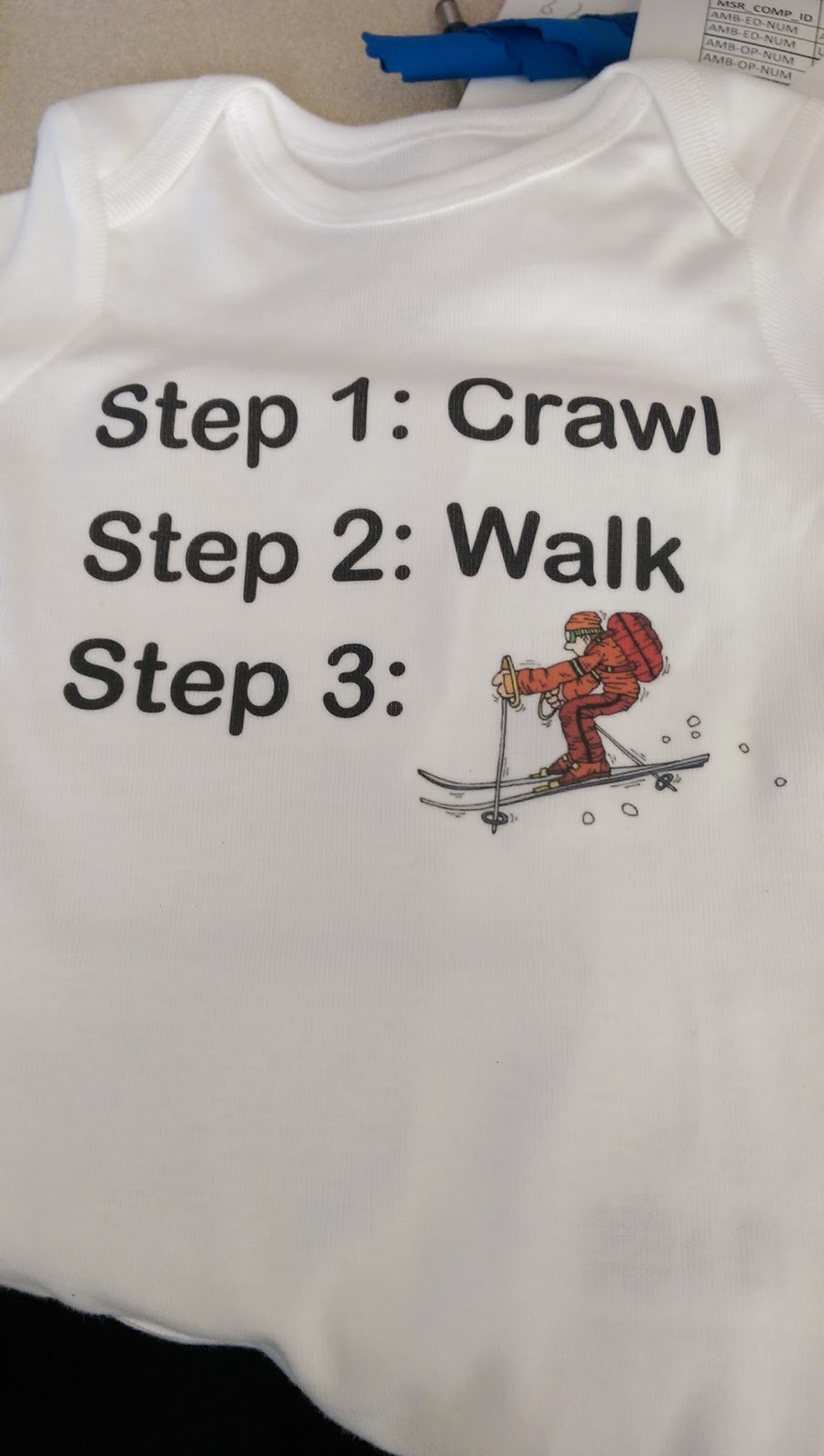 A onesie with three steps: Crawl, Walk and a picture of a guy skiing.